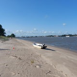 Ein Boot liegt an einem Sandstrand vor einer Industrie-Kulisse.