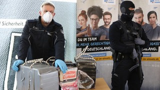 Ein Zollfahnder und ein maskierter Polizist bewachen einen großen Drogenfund