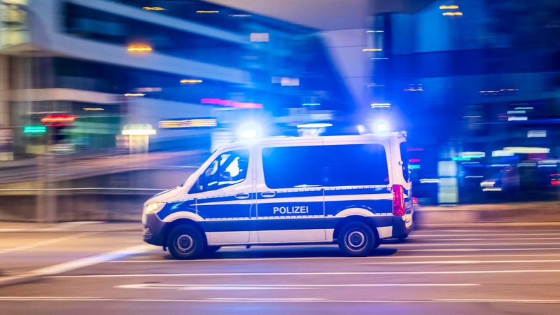 Ein Polizeifahrzeug fährt mit Blaulicht bei Nacht durch eine Stadt.