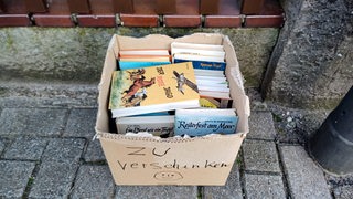 Eine Bücherkiste mit der Aufschrift "zu verschenken" steht auf dem Bürgersteig
