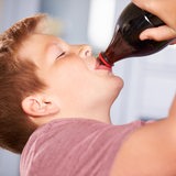Ein Junge trinkt Cola aus einer Flasche.