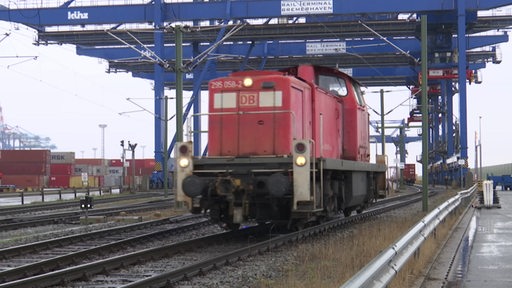 Eine rote Lok der DB fährt unter mehreren Hafenkränen hindurch.