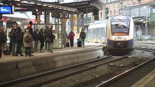 Ein Zug fährt in den Bremer Hauptbahnhof ein. Am Gleis wartende Fahrtgäste.