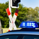 Ein Einsatzfahrzeug der Polizei steht vor einem beschrankten Bahnübergang.