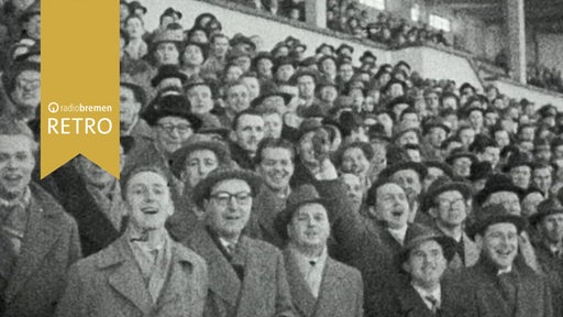 Zuschauer in Mänteln und Hüten schauen auf Spielfeld im Weser-Stadion
