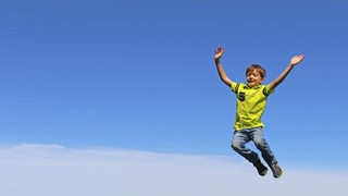 Ein Junge springt in die Luft, im Hintergrund blauer Himmel