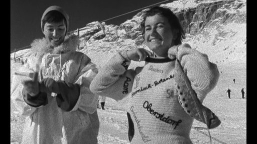 Ein schwarz-weiß Bild auf dem zwei Frauen im Skigebiet zu sehen sind. Die eine trägt einen Strickpullover.