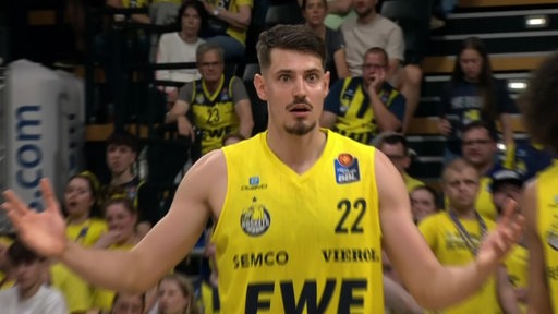 Der Oldenburger Basketballspieler Lukas Wank steht in der Sporthalle und schaut erschrocken.