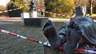Mit einem Polizeiabsperrband sind die verbleibenden Stelen der 5 gestohlenen Bronzefiguren in Bremen Osterholz umzäunt. Zwei Figuren sind erhalten.