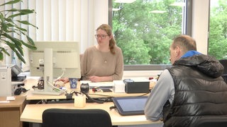 Eine Person sitzt zusammen mit einer Mitarbeiterin des Büergeramtes bei einem Termin am Schreibtisch.