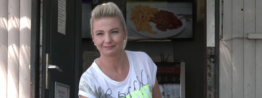 Eine blonde Frau hält einen Teller mit Essen und schaut in die Kamera.