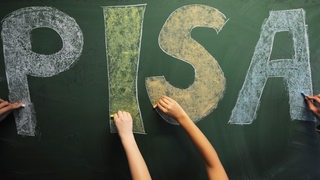Schüler*innen schreiben das Wort PISA an die Tafel