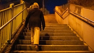 Eine Frau geht nachts eine einsame Treppe hoch.
