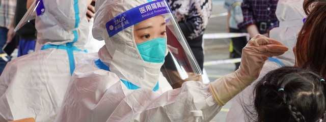 Eine chinesische Frau im Schutzanzug führt bei einer Landsfrau einen Corona-Test durch.
