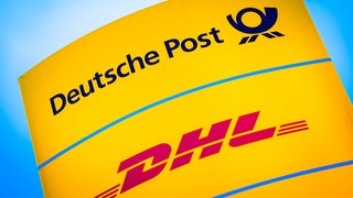Die Logos von Deutsche Post und DHL leuchten auf einem Schild vor einer Zustellbasis.