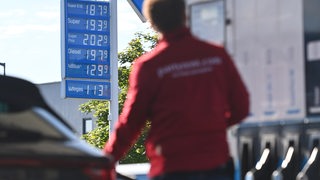 Ein Mann betankt an einer Tankstelle sein Fahrzeug und schaut auf die Preistafel (Archivbild)