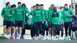 Werder-Spieler schlendern gemeinsam den Weg zum Trainingsplatz entlang.