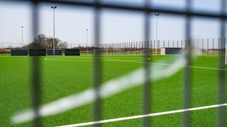 Blick auf einen leeren Fußballplatz durch einen Zaun.