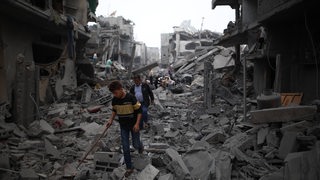 Menschen laufen im Gazastreifen über Geröll und Schutt