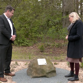 Zwei Menschen stehen an einem Gedenkstein.