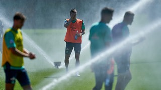 Werder-Spieler werden auf dem Trainingsplatz von Wasserfontänen nass gespritzt.