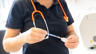 Hausärztin mit Stethoskop zieht eine Spritze auf (Symbolbild)