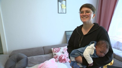 Die Hebamme Suse Werth lächelt in die Kamera und hält ein Baby im Arm.