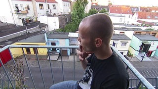 Ein Mann sitzt auf einem Balkon und raucht eine Zigarrette