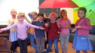 Mehrere Kinder posieren mit Regenschirmen für die Kamera.