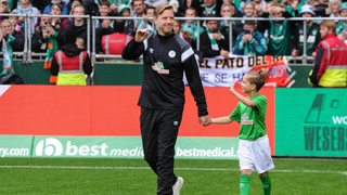 Ex-Trainer Florian Kohfeldt läuft strahlend und winkend im Weser-Stadion zum Abschiedsspiel von Claudio Pizarro ein.