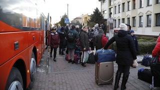 Ukrainische Geflüchtete warten vor einem Bus.