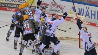 Eishockey-Spieler des EHC München bejubeln einen Treffer in den Playoffs, neben ihnen auf dem Eis enttäuschte Spieler der Fischtown Pinguins.
