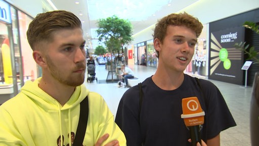 Zwei junge Männer geben in einem Kaufhaus ein Interview. 