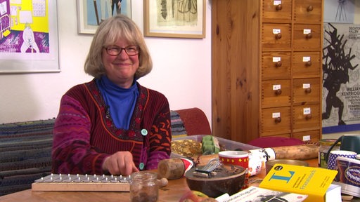 Trickfilmmacherin Ulrike Isenberg an einem Tisch mit vielen bunten Gegenständen bei sich zu Hause.
