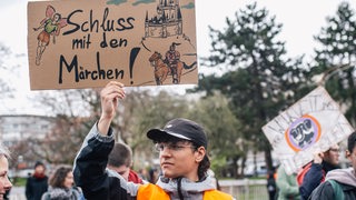 Ein Mensch mit einem Protestschild mit der Aufschrift: "Schluss mit dem Märchen"