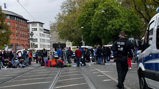 Eine Gruppe von Demonstrierenden auf einer Kreuzung, im Vordergrund ein Polizist