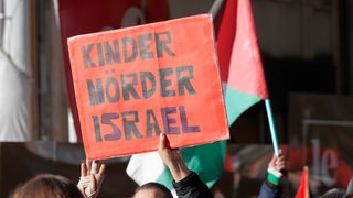 Eine Person hält auf einer Demonstration ein Schild in die Höhe. Auf dem steht: "Kinder Mörder Israel."