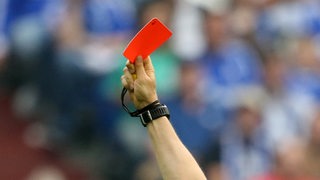 Eine Rote Karte wird von der Hand eines Schiedsrichters in die Luft gestreckt