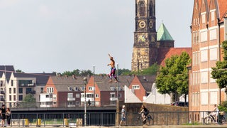 Ein Slackliner balanciert auf einem Seil in Bremen, Stephanieviertel, über die Weser. Im Hintergrund die Stephaniekirche.