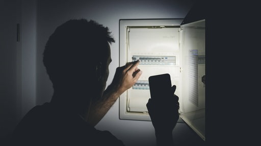 Ein Mann schaut sich den Stromkasten an und leuchtet mit seinem Handy