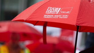 Ein roter Schirm mit der Aufschrift "Ohne uns kein Geschäft" ist auf einer Kungebung der Gewerkschaft Verdi zu sehen