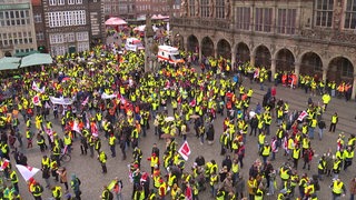 Demonstrierende Menschen in gelben Warnwesten und mit Ver.di-Flaggen  auf dem Bremer Marktplatz. 
