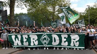 Werder-Fans laufen über eine Straße. Sie tragen ein Transparent mit der Aufschrift "Werder" vor sich her.