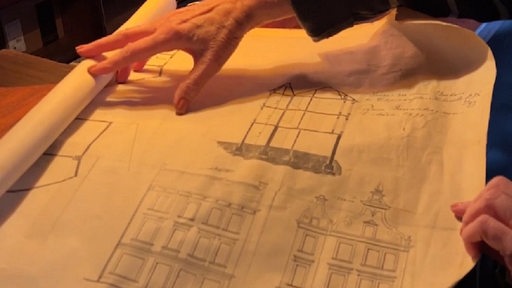 Eine Hand rollt eine Skizze von einem Gebäude aus