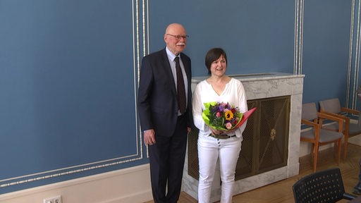 Der Innensenator Ulrich Mäurer (SPD) ist neben der mutigen Bremerin Ute Kraft-Uhlhorn, welche einen Blumenstrauß in den Händen hölt, zu sehen.